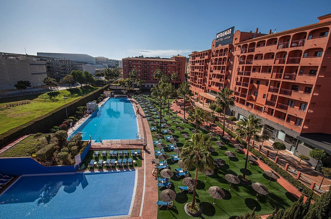 Uteområde ved NHFH Campus Spania med stort basseng, solsenger, palmer og leilighetsbygg i Fuengirola på Costa del Sol﻿