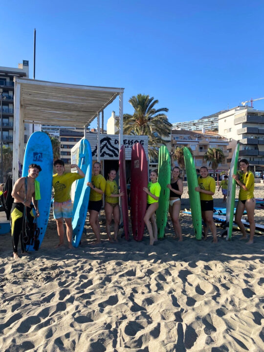 Studenter står på stranden med surfebrett under surfekurs ved kysten i Fuengirola